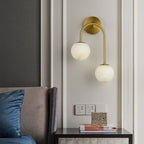 Brass Clérachic Two-Globe Alabaster Wall Sconce on a panelled bedroom wall, freeing the bedside table below for books and a small box.