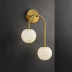 Clérachic Two-Globe Alabaster Wall Sconce in polished brass against a dark charcoal wall, the pale stone globes standing out in contrast.