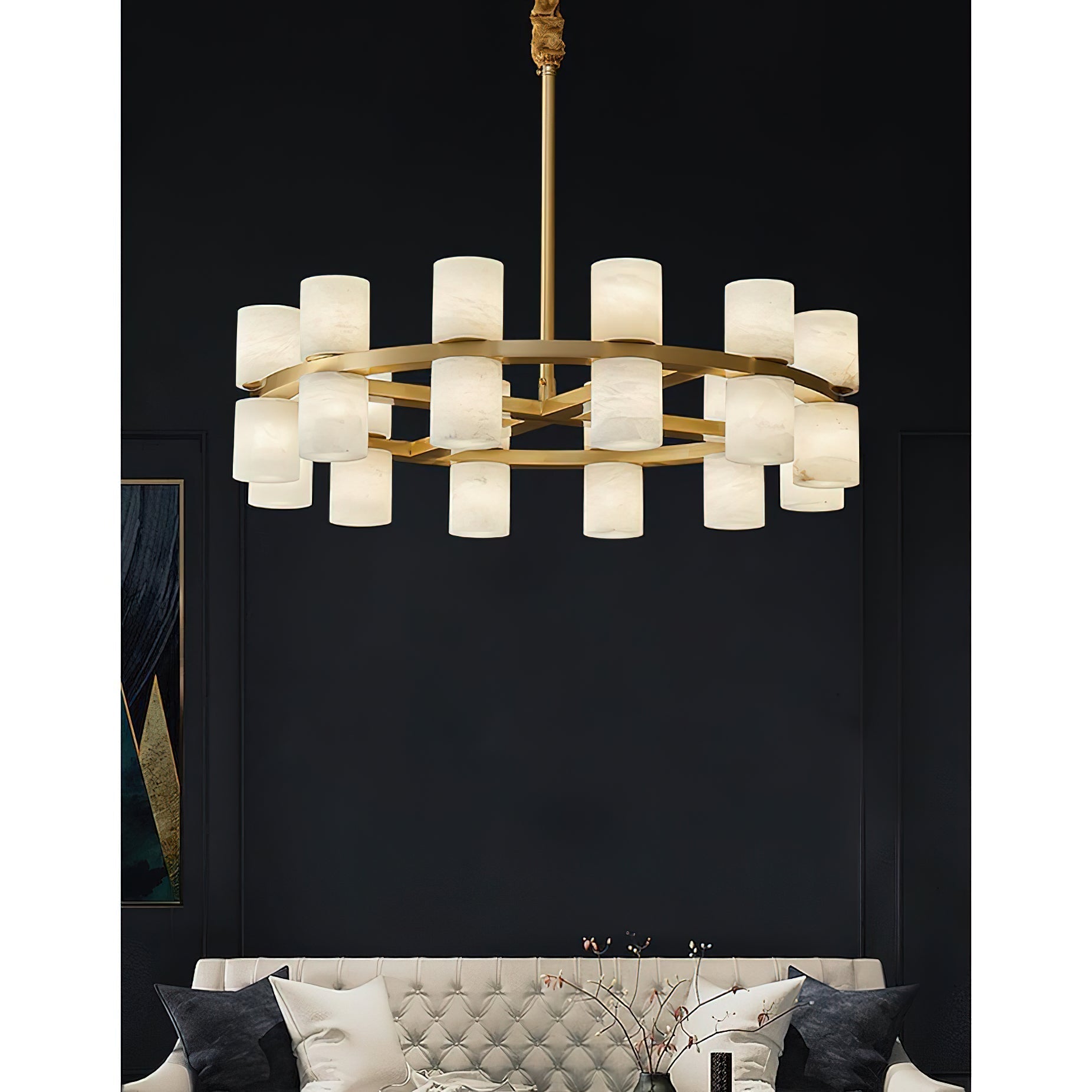 The Clérachic Two-Ring Chandelier on its rigid brass rod, seen head-on above a cream buttoned sofa in a dark room.