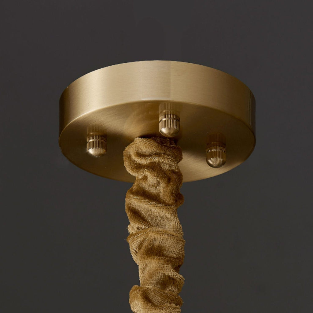 Close-up of the Clérachic chandelier's round brass canopy, three knurled screws and the gathered ochre velvet sleeve.