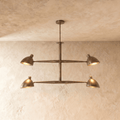 Clérachic chandelier in vintage brass, four cone shades on a crossbar frame beneath a plaster ceiling.