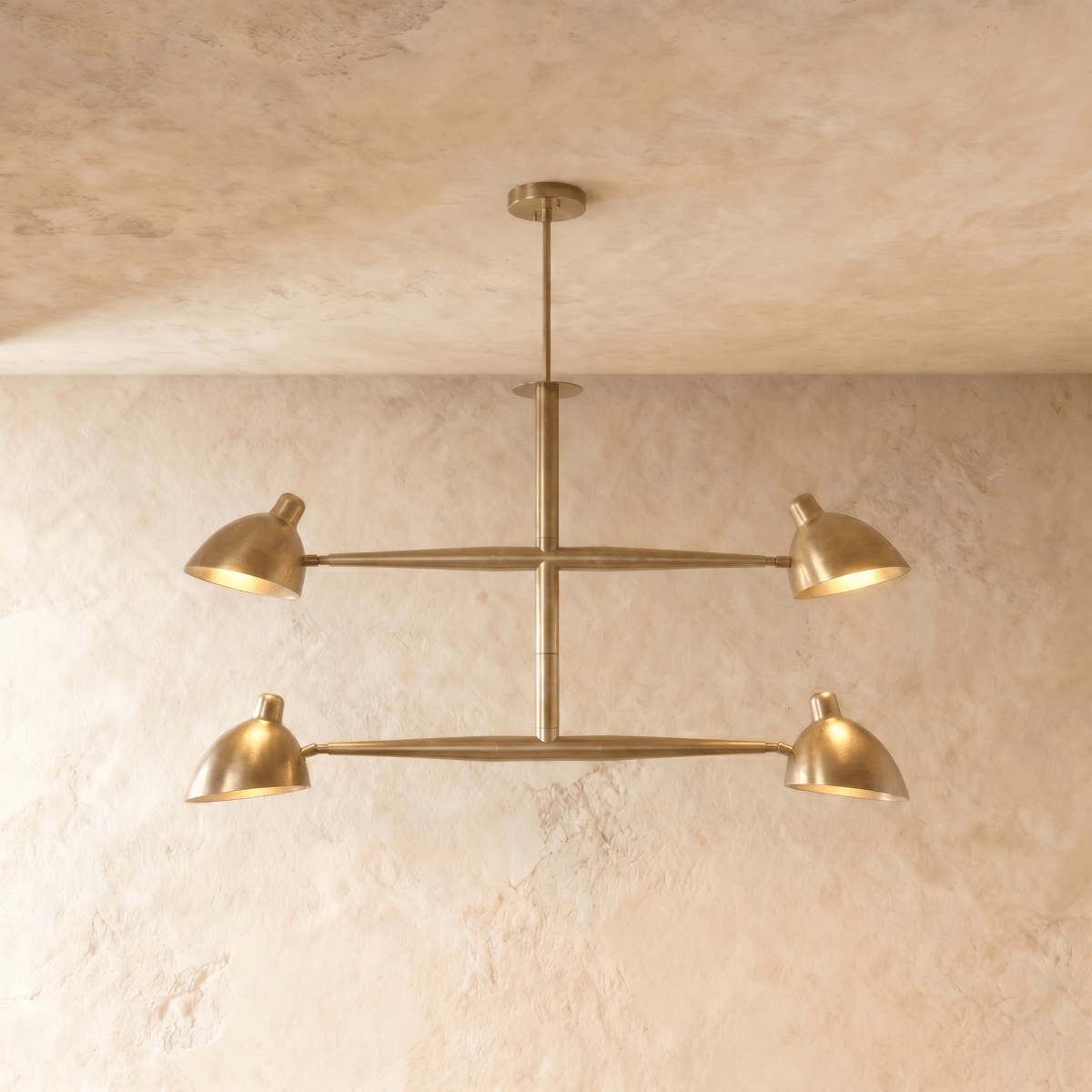 Clérachic chandelier in brushed brass, four cone shades on a crossbar frame beneath a plaster ceiling.
