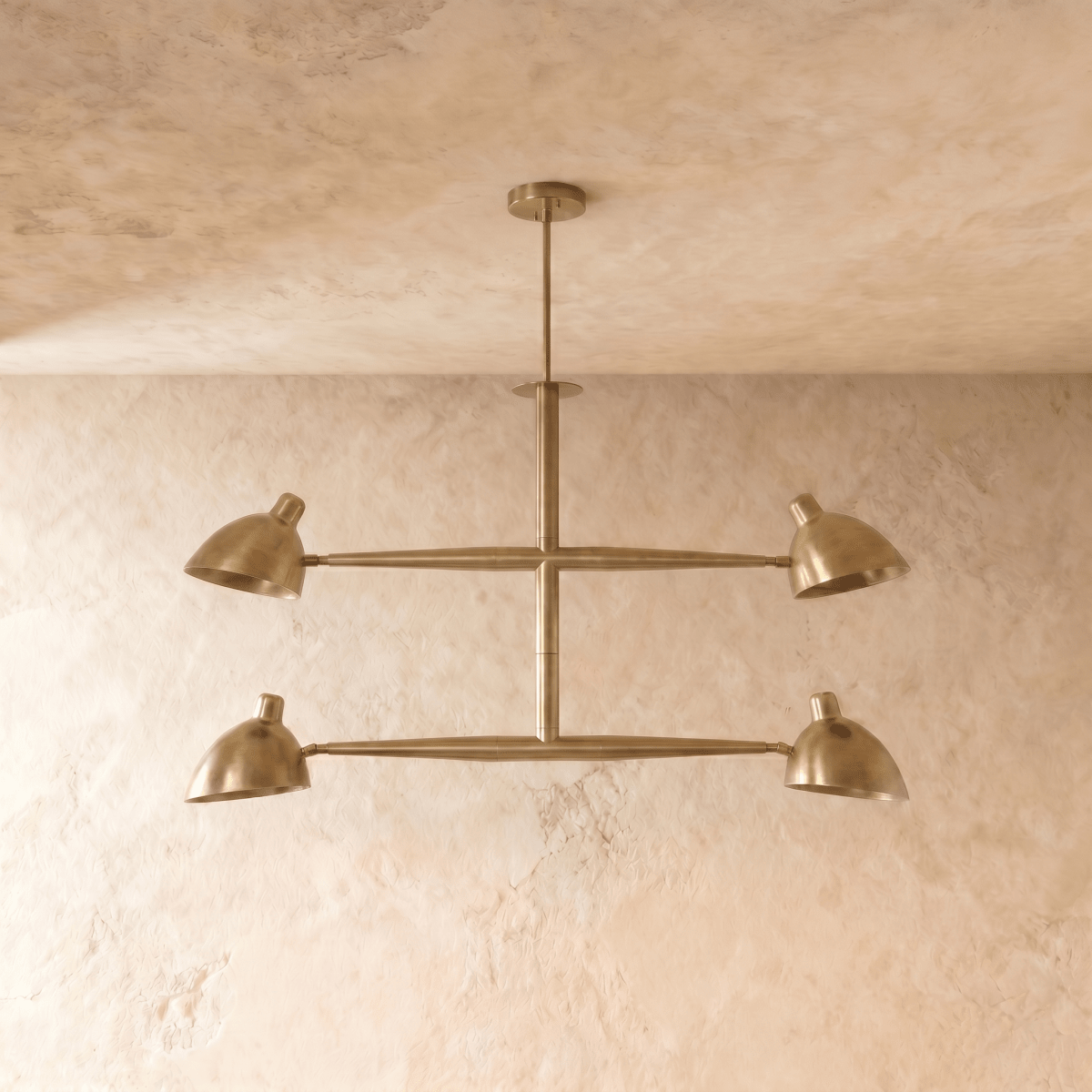 Clérachic chandelier in brushed brass shown from another angle, its crossbar arms catching warm light.