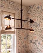 Clérachic chandelier in matte black shown close against floral wallpaper beside a garden-view window.