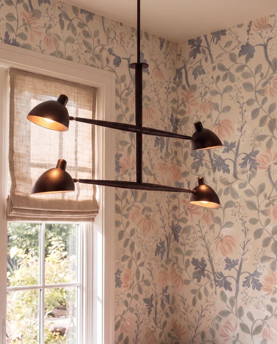 Clérachic chandelier in matte black shown close against floral wallpaper beside a garden-view window.