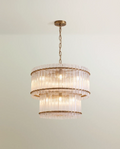 Clérachic two-tier chandelier in antiqued brass with fluted clear glass rods, hung from a chain against a pale green wall.
