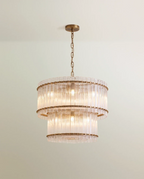Clérachic two-tier chandelier in antiqued brass with fluted clear glass rods, hung from a chain against a pale green wall.