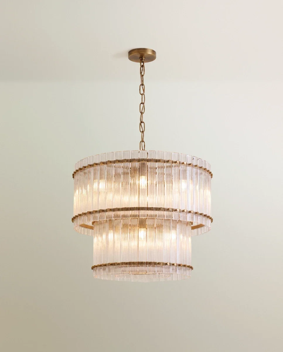 Clérachic two-tier chandelier in antiqued brass with fluted clear glass rods, hung from a chain against a pale green wall.