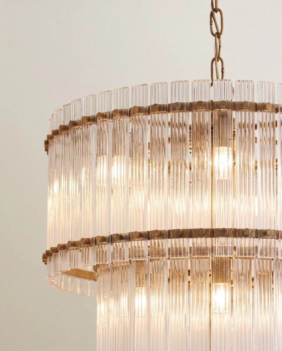 Clérachic close view of the antiqued brass chandelier, showing fluted glass rods clipped to riveted metal bands over lit bulbs.