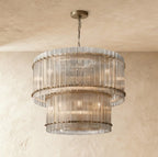 Clérachic two-tier chandelier with antiqued brass fittings and fluted clear glass, hung against a textured plaster wall.