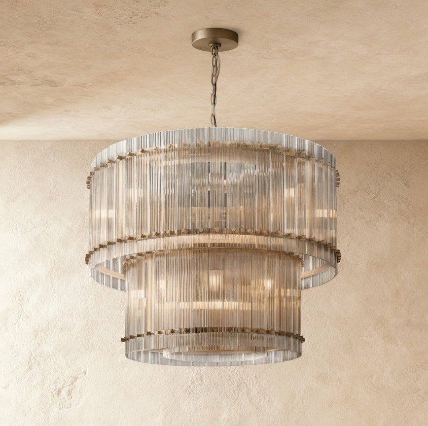 Clérachic two-tier chandelier with antiqued brass fittings and fluted clear glass, hung against a textured plaster wall.