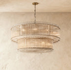 Clérachic wide two-tier chandelier with fluted clear glass rods and metal bands, hung on a chain against textured plaster.