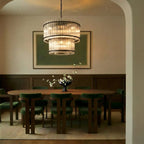 Clérachic matte black two-tier chandelier glowing over an oval walnut dining table with green velvet chairs.