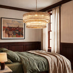 Clérachic large antiqued brass two-tier chandelier hung low above a bed with olive linen, in a panelled bedroom.