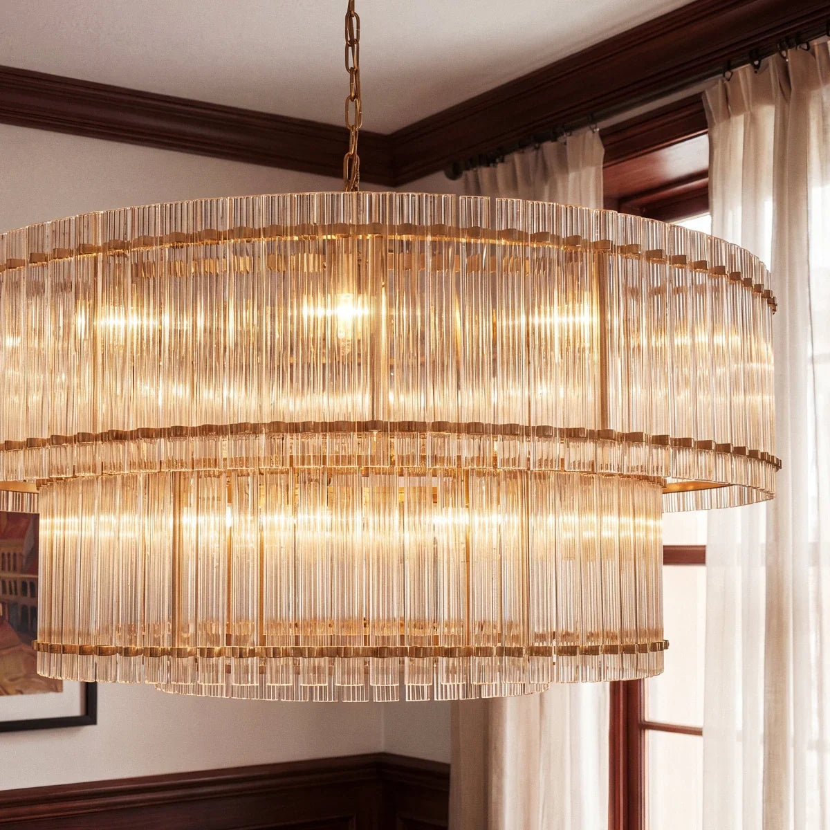 Clérachic close view of the antiqued brass chandelier, with fluted glass rods and brass bands beside a window with sheer curtains.
