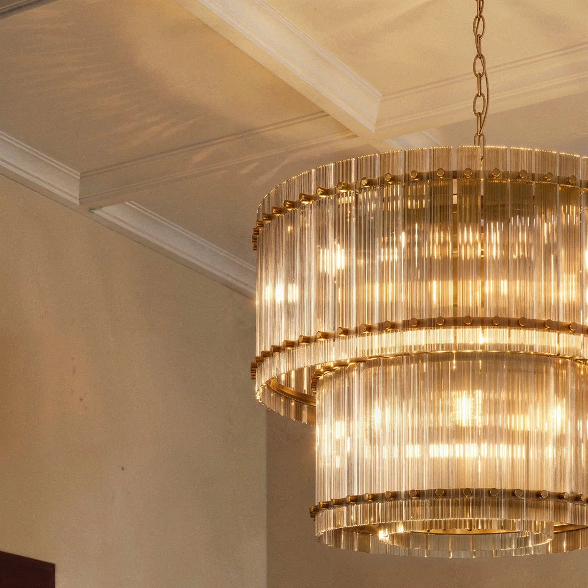 Clérachic close view of the antiqued brass chandelier, warm light shining through two tiers of fluted glass under a coffered ceiling.