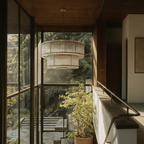 Clérachic antiqued brass two-tier chandelier hung in a glazed stairwell with a timber ceiling and trees outside.