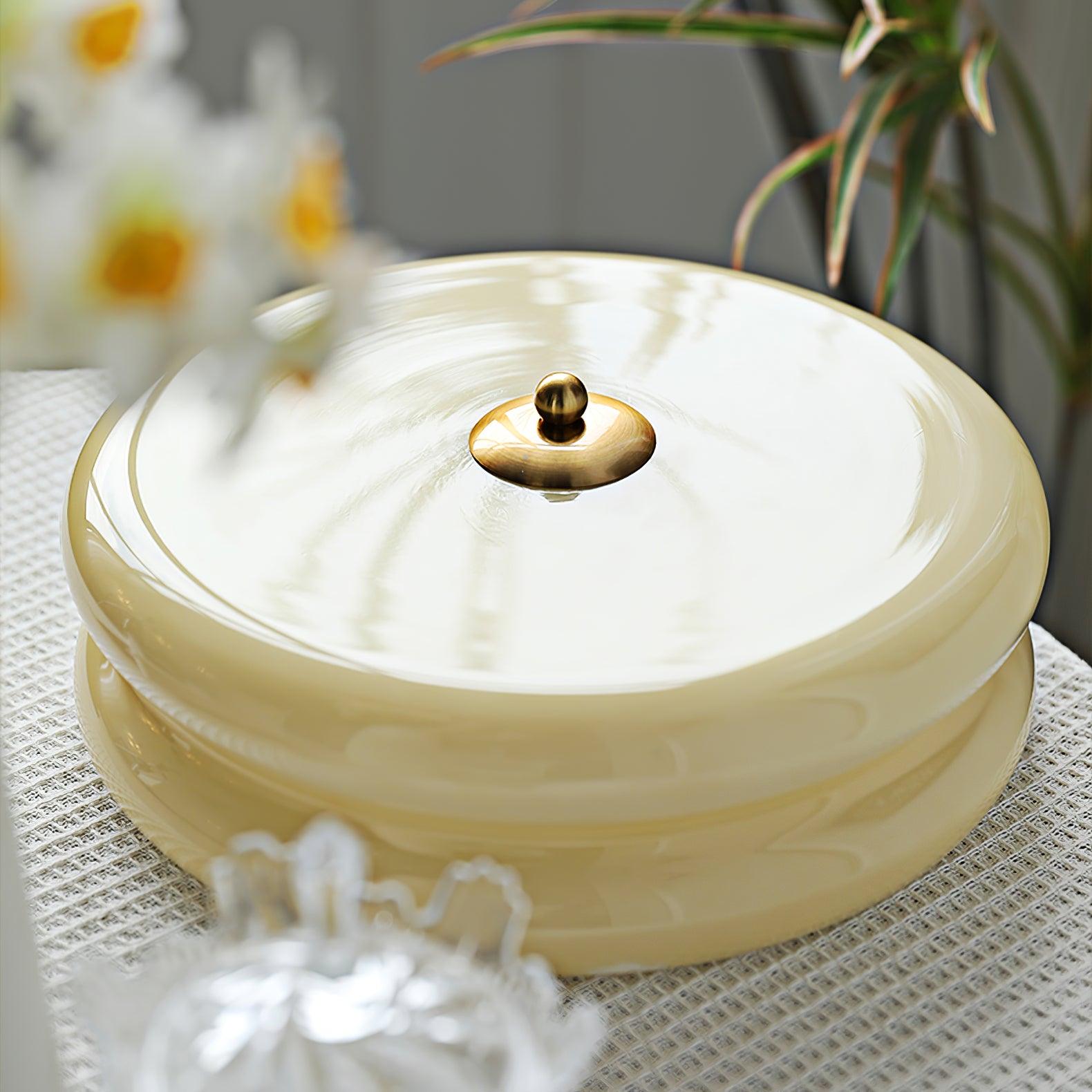 Clérachic two-tier flush mount ceiling light photographed on a table, cream glass and brass finial beside white flowers.