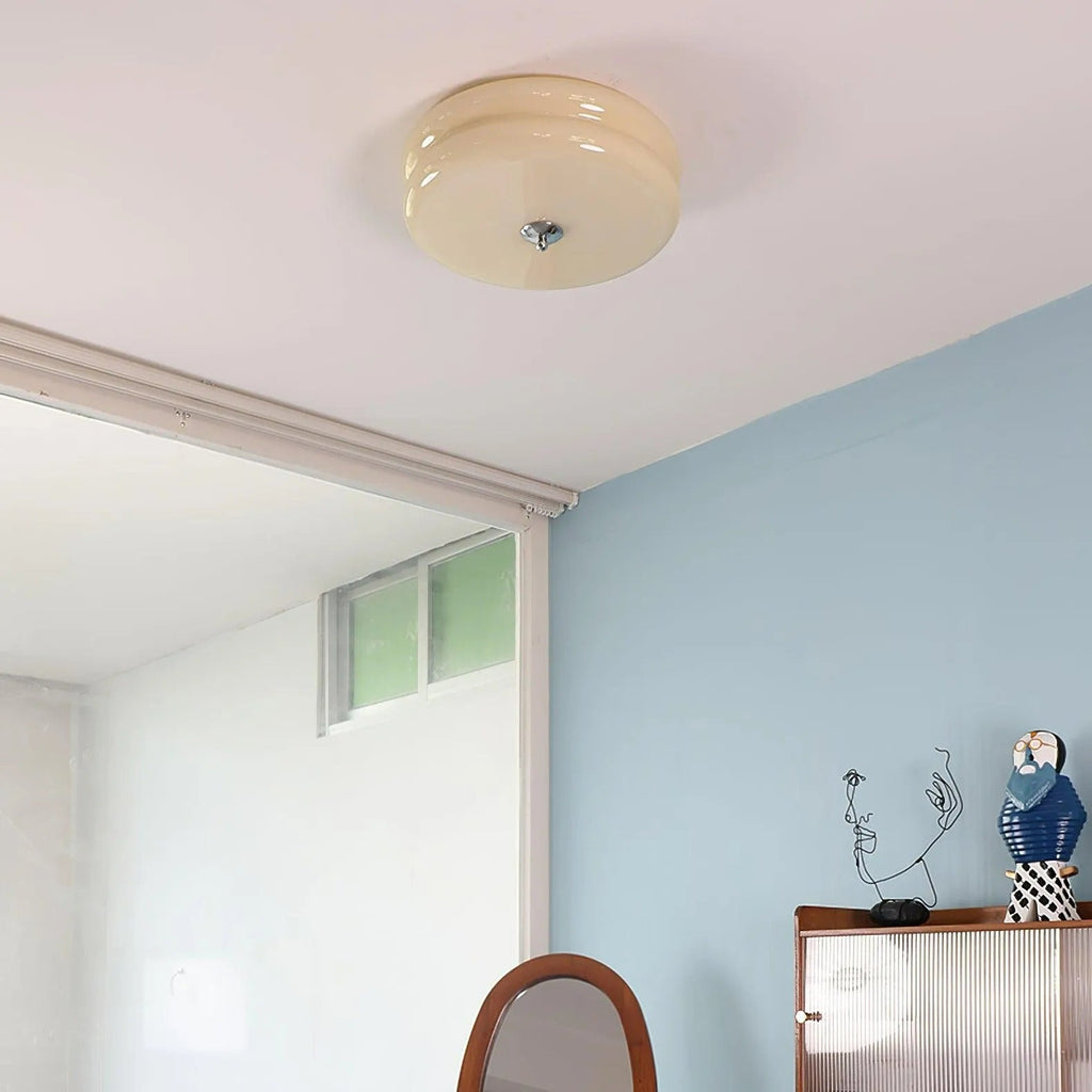 Beige Clérachic two-tier flush mount ceiling light on a white ceiling above a blue bedroom wall and reeded cabinet.