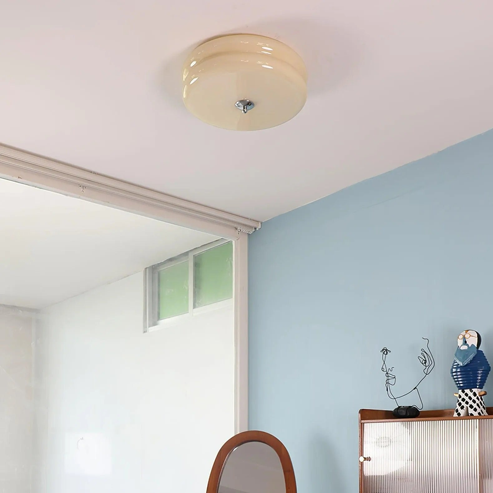 Beige Clérachic two-tier flush mount ceiling light on a white ceiling above a blue bedroom wall and reeded cabinet.