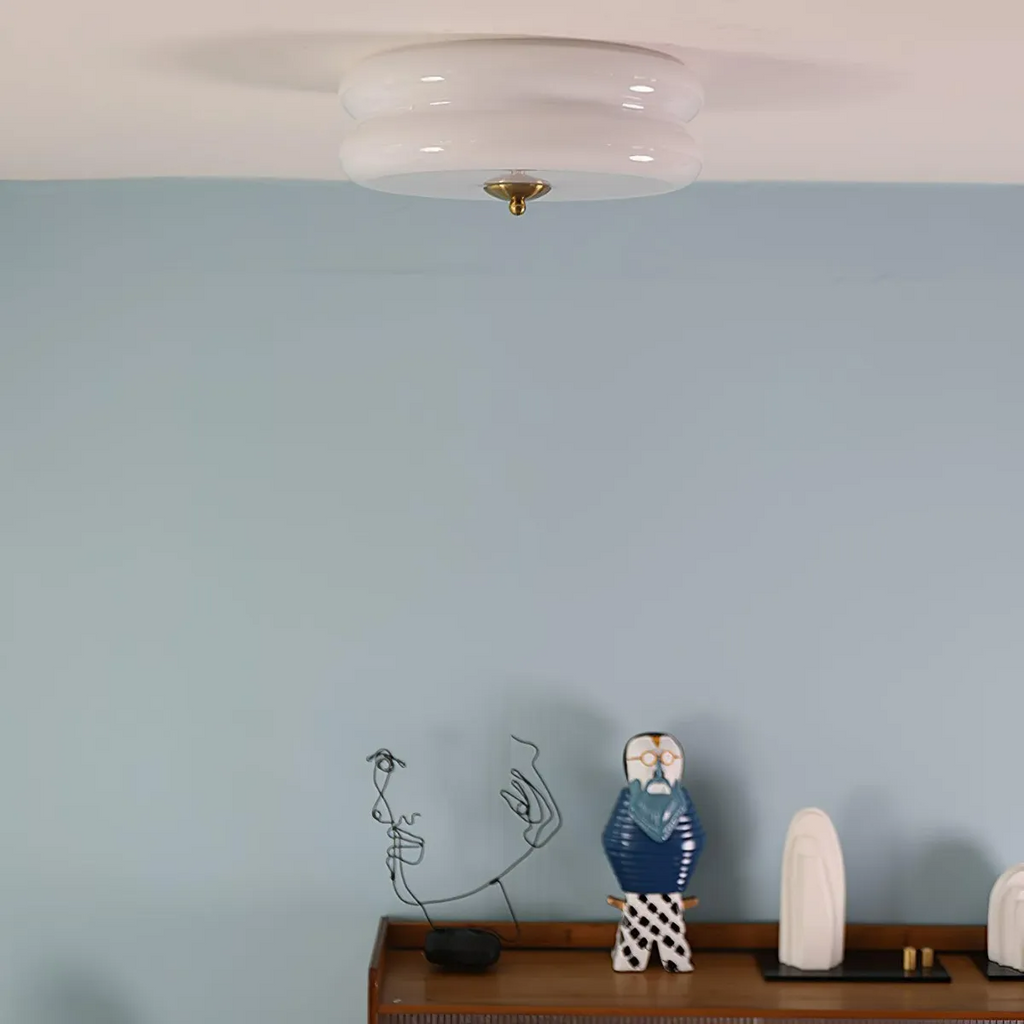 White glass Clérachic two-tier flush mount ceiling light and brass finial above a blue wall and wooden sideboard.