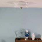 White glass Clérachic two-tier flush mount ceiling light and brass finial above a blue wall and wooden sideboard.