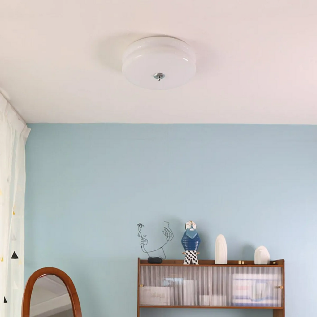 Clérachic two-tier flush mount ceiling light in white glass lighting a blue bedroom with a mirror and reeded cabinet.