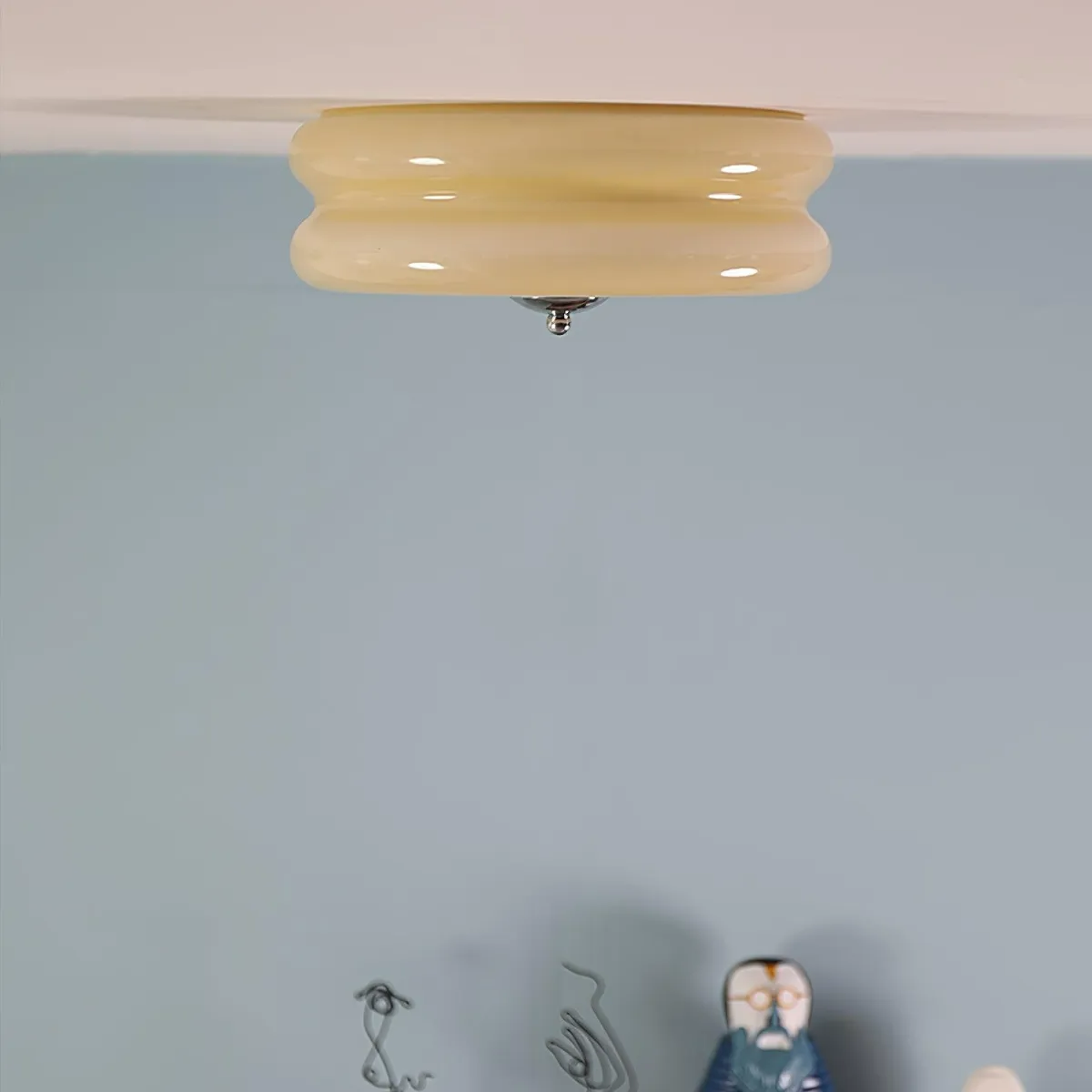 Close crop of the beige Clérachic two-tier flush mount ceiling light at the ceiling edge above a soft blue wall.