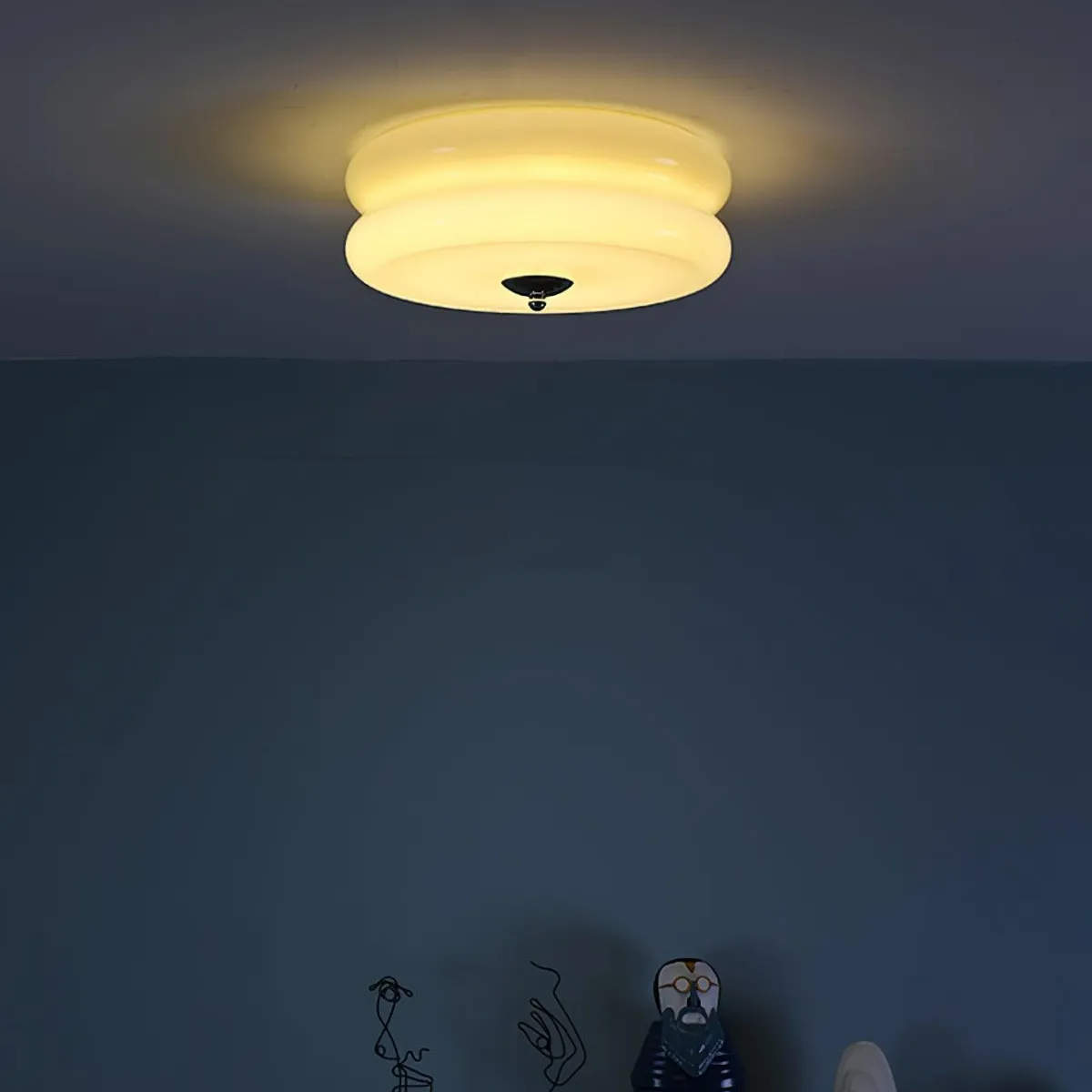 Clérachic two-tier flush mount ceiling light lit at night, warm glow spilling across the ceiling above a dark wall.
