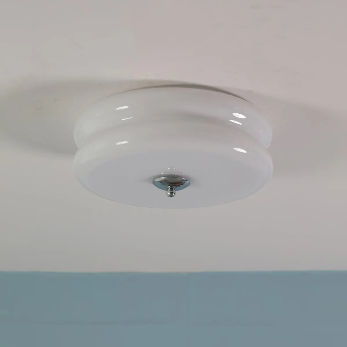 White Clérachic two-tier flush mount ceiling light unlit on a white ceiling, a blue wall running below it.