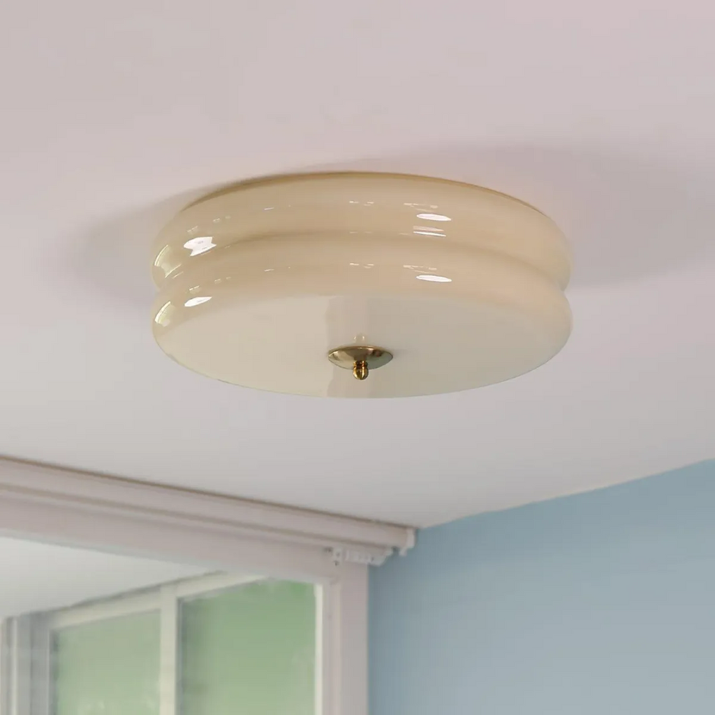 Beige Clérachic two-tier flush mount ceiling light with a brass finial, mounted near a window in a blue room.