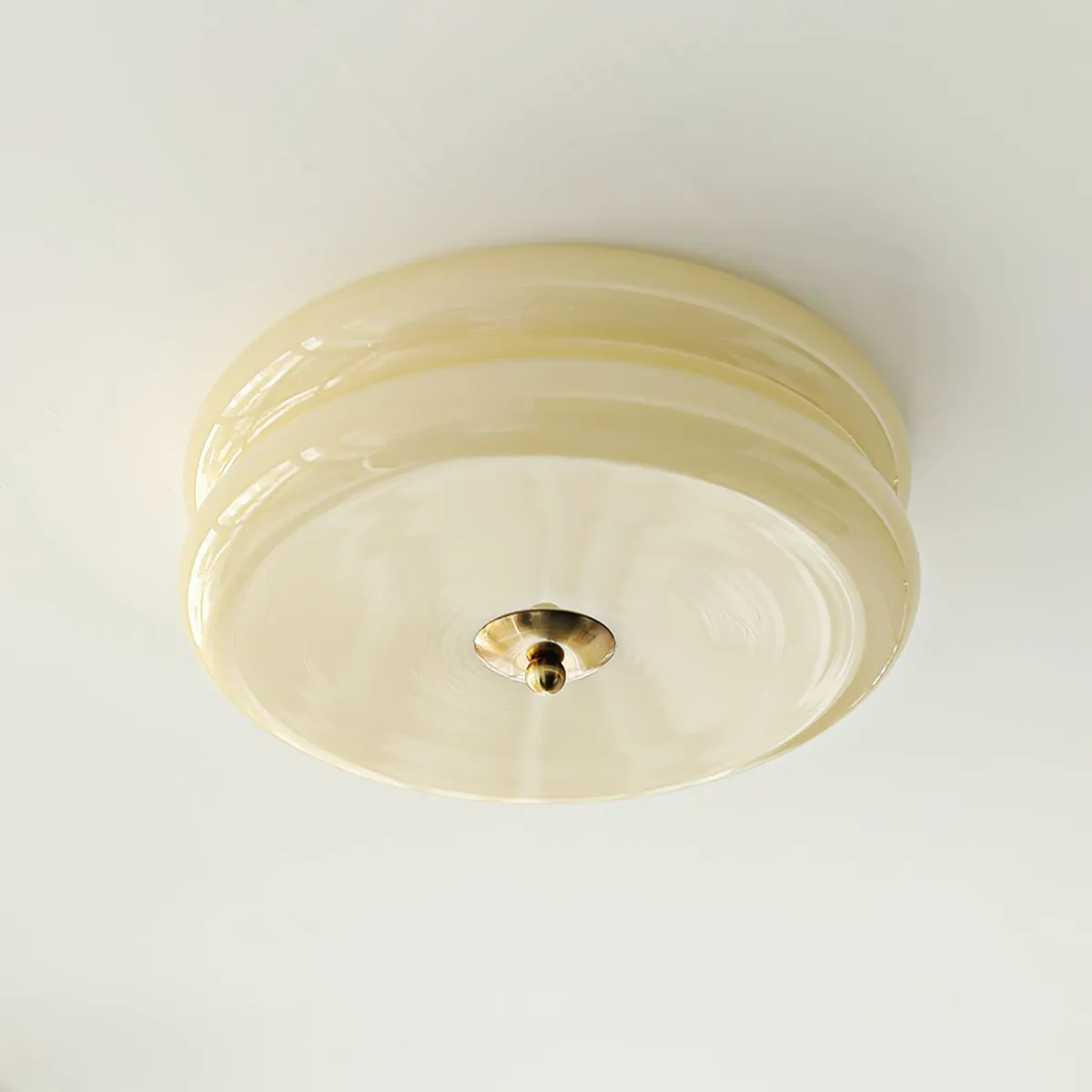 Clérachic two-tier flush mount ceiling light viewed straight from below, brass finial centred on the cream glass.