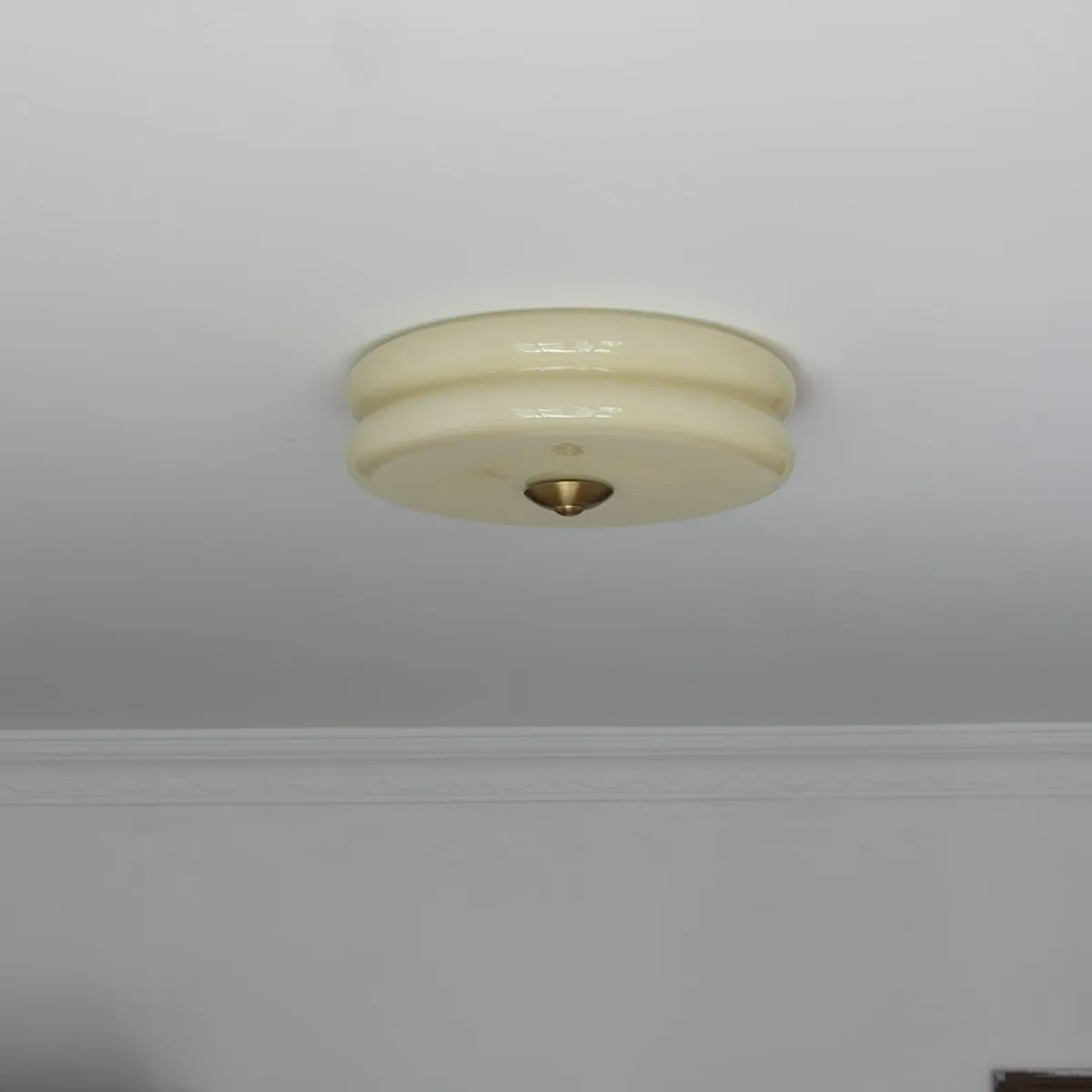 Small beige Clérachic two-tier flush mount ceiling light on a white ceiling beside a moulded plaster cornice.