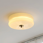 Clérachic two-tier flush mount ceiling light lit in cream glass, brass finial above a curtain rail and window.