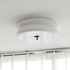 White glass Clérachic two-tier flush mount ceiling light with a chrome finial above sheer curtains at a window.