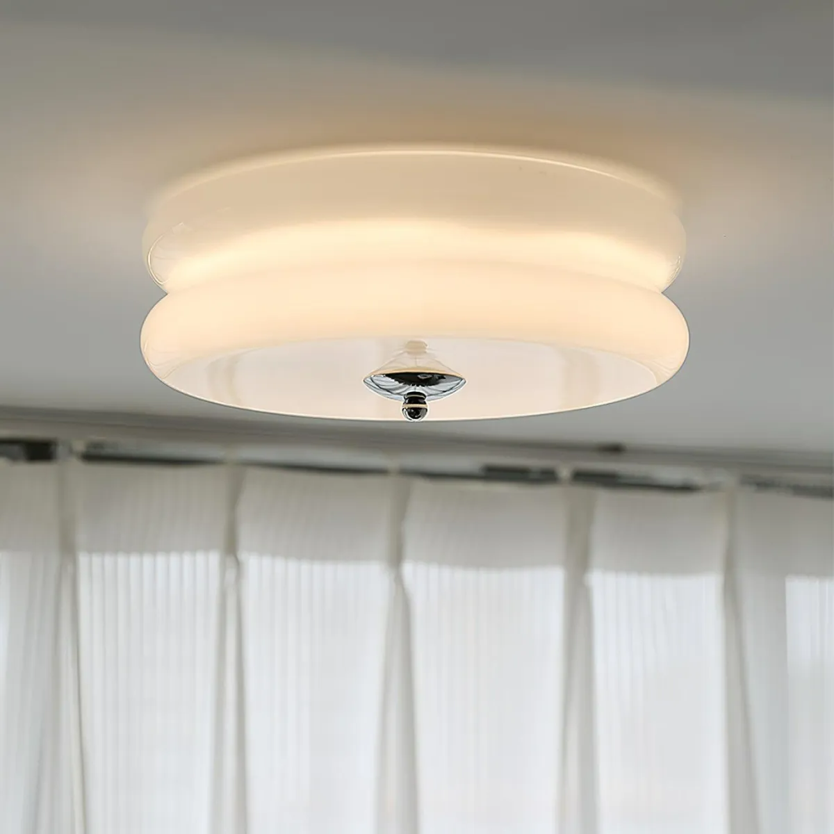 Lit Clérachic two-tier flush mount ceiling light in white glass, chrome finial glowing above sheer curtains.