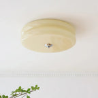 Beige Clérachic two-tier flush mount ceiling light above a dentil cornice, with a green plant in the foreground.