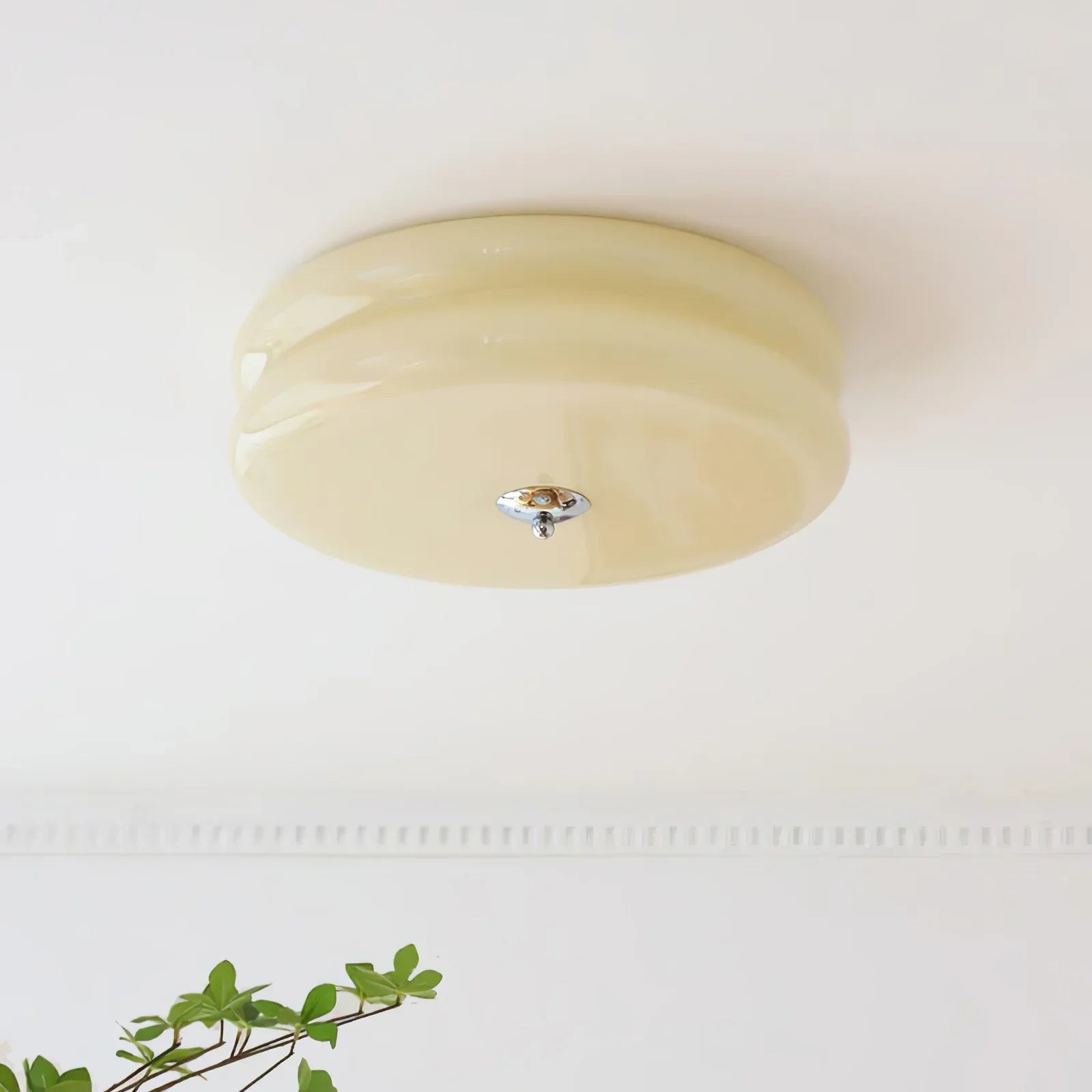 Beige Clérachic two-tier flush mount ceiling light above a dentil cornice, with a green plant in the foreground.