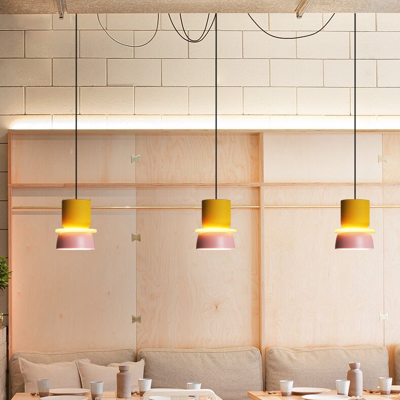 Three Clérachic two-tone dome pendants in yellow and mauve-pink hang at staggered heights over a dining banquette.