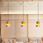 Three Clérachic two-tone dome pendants in yellow and mauve-pink hang at staggered heights over a dining banquette.
