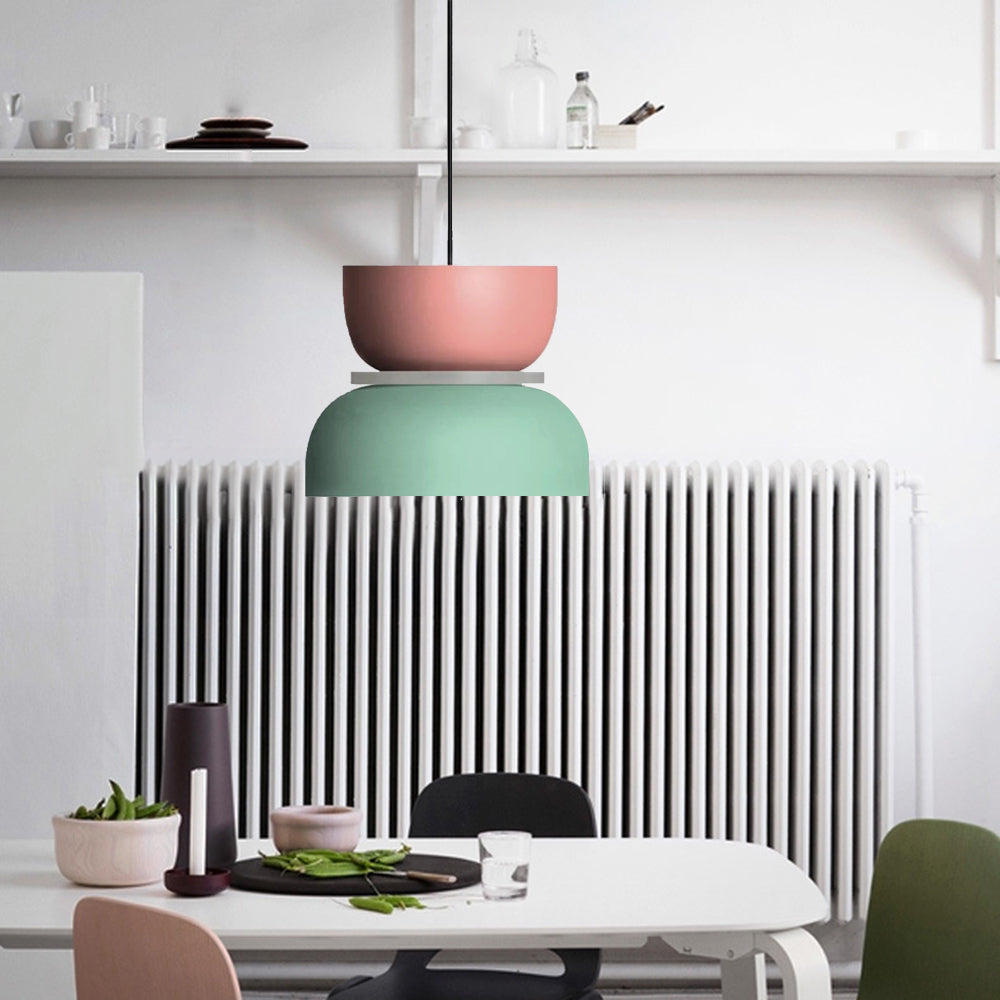 A Clérachic two-tone dome pendant in pink and mint green hangs above a dining table in front of a white radiator.