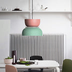 A Clérachic two-tone dome pendant in pink and mint green hangs above a dining table in front of a white radiator.