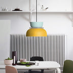 A Clérachic two-tone dome pendant in mint blue and yellow hangs over a dining table beside a kitchen radiator.