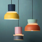 Three Clérachic two-tone dome pendants in navy-yellow, pink-charcoal and mint-orange hang against a teal wall.