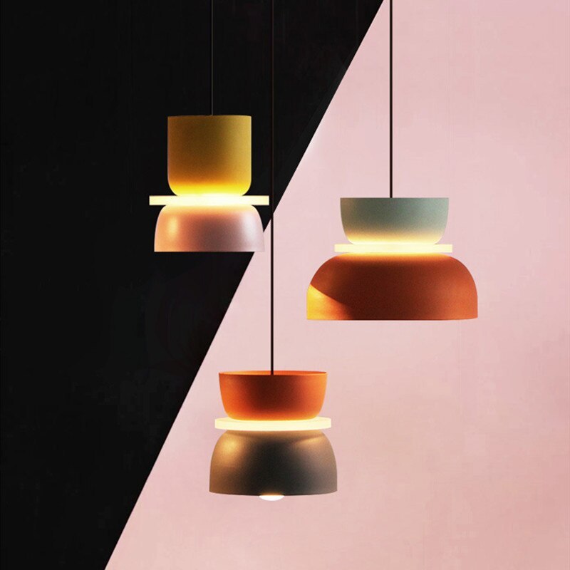 Three Clérachic two-tone dome pendants in yellow-mauve, mint-orange and orange-charcoal float against a graphic pink and black backdrop.