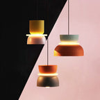 Three Clérachic two-tone dome pendants in yellow-mauve, mint-orange and orange-charcoal float against a graphic pink and black backdrop.