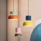 Three Clérachic two-tone dome pendants in mint-orange, navy-yellow and pink-charcoal hang against a warm stone wall.