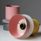 Disassembled Clérachic two-tone dome pendant parts — pink upper cup, frosted diffuser disc and yellow lower dome — laid on a table.