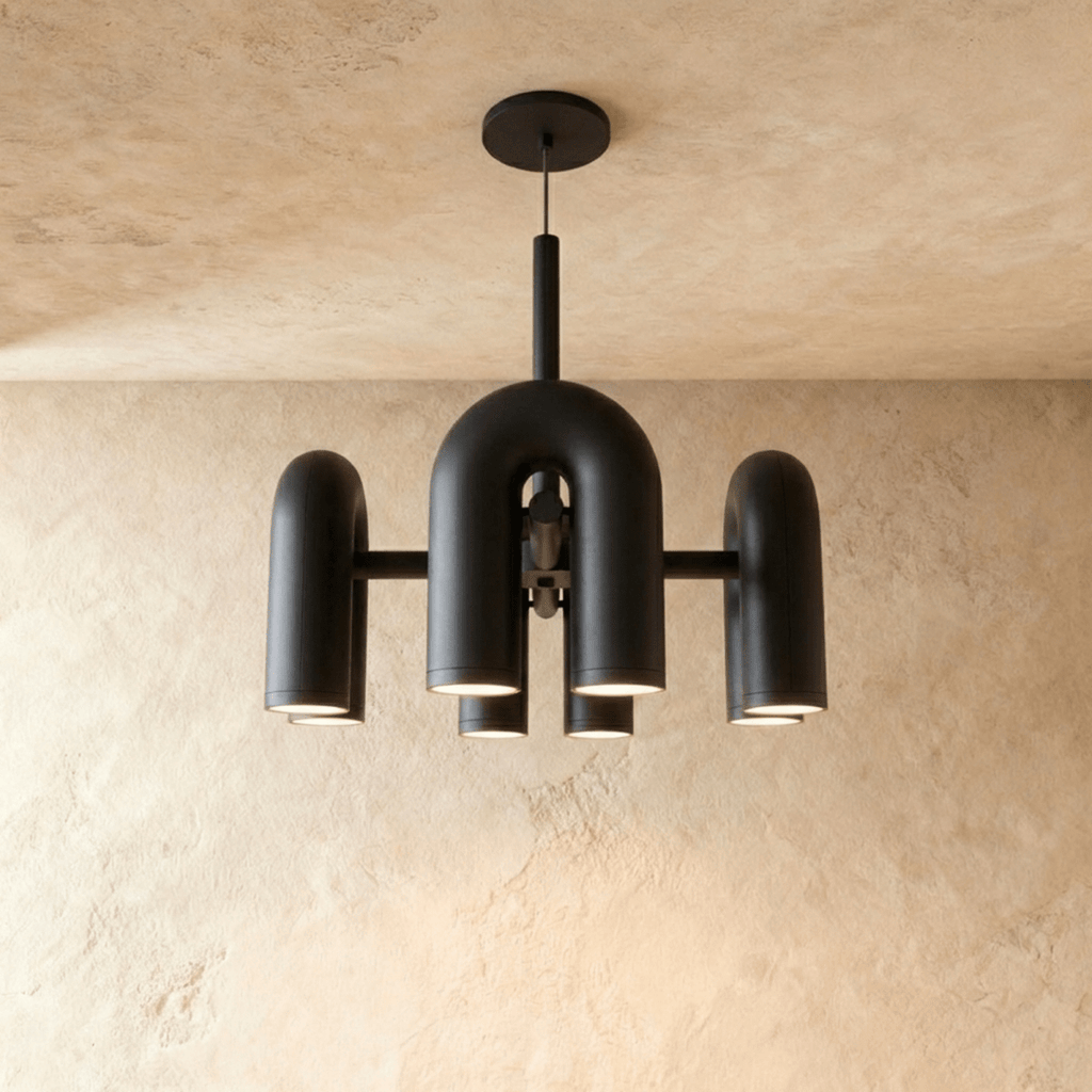 Clérachic chandelier of rounded U-shaped modules in matt black, hung from a round ceiling plate against a limewashed plaster wall.