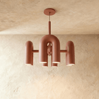 Clérachic chandelier of rounded U-shaped modules in terracotta orange, lit from below against a limewashed plaster wall.